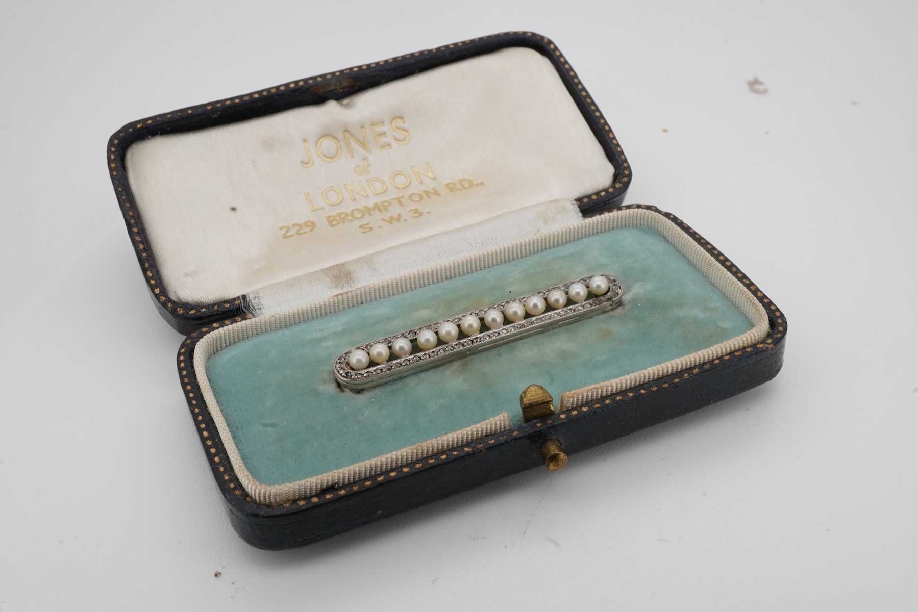 A Belle Epoque pearl and diamond brooch, early 20th century, of bar design, composed of a line of seed pearls within an oval border of rose-cut diamonds, mounted in platinum, length 3.9cm, French sponsor's mark, partial